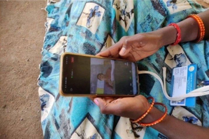 एक औरत की तस्वीर जिसमें वह अपने हाथ में मोबाइल फ़ोन पकड़े हुए है जिसपर एक वीडियो चल रहा है। हम उसकी साड़ी देख सकते हैं, उसके हाथ में चूड़ियाँ हैं और गले में परिचय पत्र लटक रहा है। जब हम डिजिटल लर्निंग से वापस स्कूल जाकर पढ़ने के पुराने तरीक़े पर लौटेंगे तब उस स्थिति में सरकारी स्कूलों और शिक्षकों के लिए अनुकूल वातावरण बनाने के लिए नीति निर्माता किस तरह के कदम उठा सकते हैं_शिक्षक