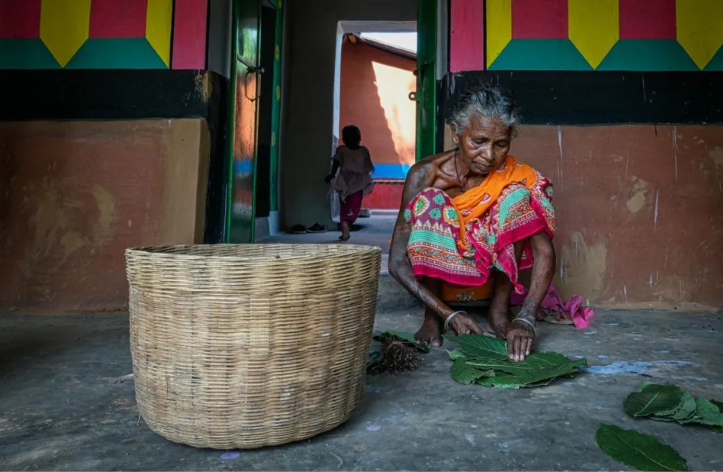 आंगन में बैठकर काम करती महिला_आदिवासी