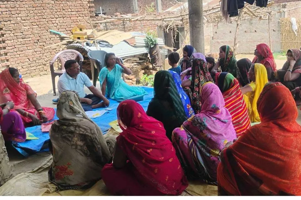 जमीन पर घेरे में बैठकर चर्चा करती महिलाएं और पुरुष_आजीविका