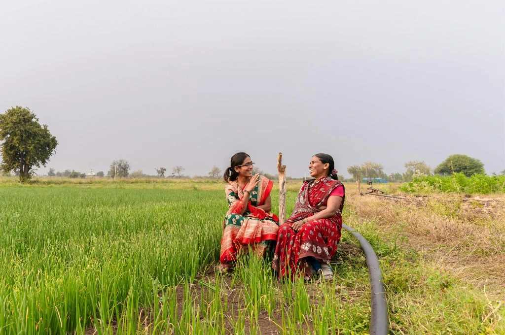 हरे-भरे खेत में बैठ कर हंसी ठिठोली करती दो महिलाएं_आशा कार्यकर्ता